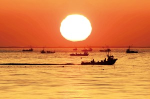サロマ湖に浮かぶ漁船の奥に大きな太陽